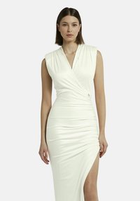 Abito bianco senza maniche in un tessuto morbido, con una design avvolgente, dettagli arricciati e uno spacco alto fino alla coscia su un lato.