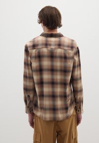 Camicia a quadri marrone e beige con maniche lunghe, colletto a punta, taschino singolo sul petto e polsini con bottoni. Tessuto casual e vestibilità rilassata.