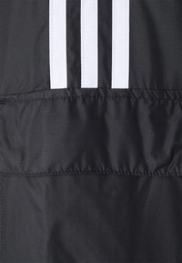 Svart tyg med tre vertikala vita ränder sydda nära toppen, som visar sömmar och textur av ett plagg.