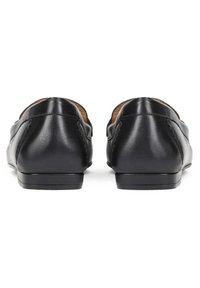 Pereche de pantofi slip-on din piele neagră, văzuți din spate, cu toc rotunjit și talpă joasă stratificată, pe fundal alb.