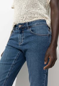 Jean en denim bleu avec une coupe classique, doté d'une fermeture à bouton, de poches avant et de surpiqûres contrastantes. Porté avec un haut en tricot léger.