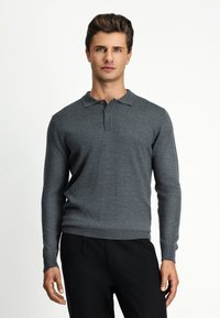 Szara longsleeve polo wykonana z miękkiego materiału, z kołnierzykiem i trzema guzikami, w zestawieniu z czarnymi spodniami.