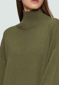 Olivgrüner Rollkragenpullover aus weichem Strickmaterial; verfügt über einen gerippten Kragen und eine lockere Passform mit gesenkten Schultern.