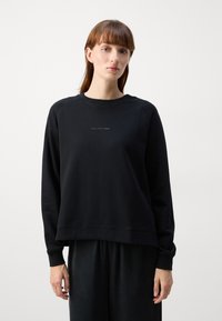 Sudadera negra con cuello redondo, puños acanalados y dobladillo. Presenta un pequeño texto del logo en el pecho. Tejido suave con un ajuste relajado.