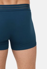 Modré boxerky s přiléhavým střihem, hladkou texturou a elastickým pasem se třemi tenkými zlatými pruhy.