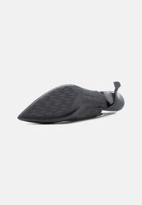 Zapato de tacón alto negro con punta afilada. Material superior suave, suela de goma texturizada con patrón geométrico y una correa trasera para mayor soporte.