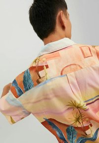 Camicetta a maniche corte realizzata in un tessuto pastello con motivi tropicali, comprese foglie e forme geometriche in tonalità di rosa, blu e giallo.