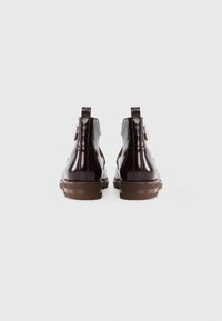 Brown leather ankle boots with a shiny finish, low heel, and side straps for closure. Textured sole for grip. Back view.