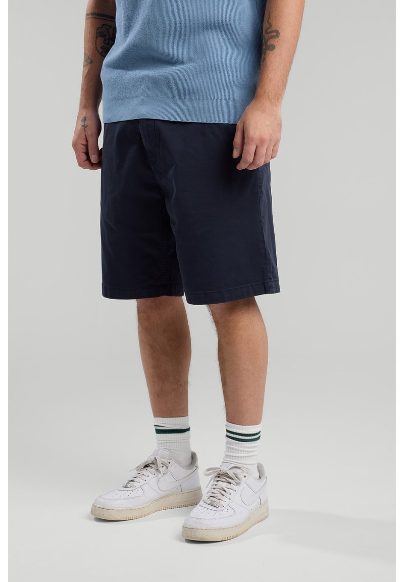 Navy blue cotton shorts with a relaxed fit, featuring side pockets, paired with white sneakers and green-striped socks.