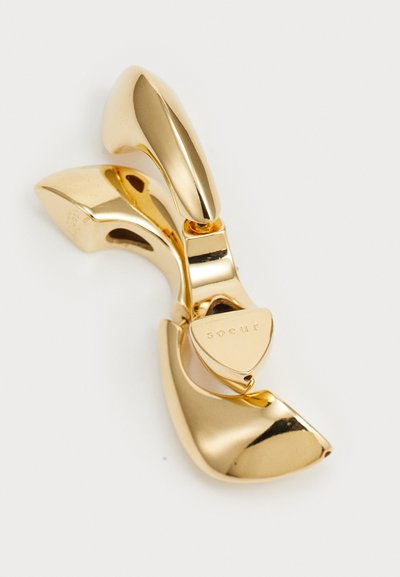 Goldfarbener Haarklammer mit elegantem, geschwungenem Design. Verfügt über einen auffälligen drehbaren Bereich und eingravierten Markennamen auf der Unterseite.