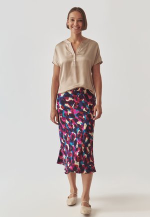 Beige satinbluse med knaplukning ved halsen og korte ærmer, parret med en farverig mønstret midi-nederdel med nuancer af pink og blå.