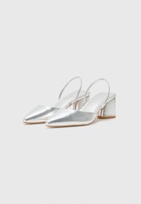 Silverfärgade metallic slingback-skor med spetsig tå och blockklack. Slät textur med ankelrem.