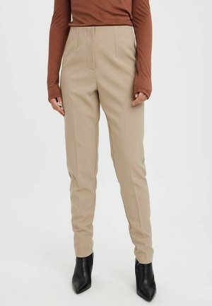 Rechte beige broek gedragen met een roestkleurige top met lange mouwen en zwarte enkellaarsjes met een spitse neus op een witte achtergrond.