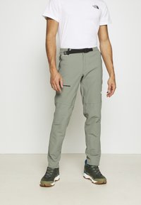 Lekkie, oliwkowe spodnie outdoorowe z paskiem, kieszeniami na zamek i zwężonym krojem. Noszone z wielokolorowymi butami trekkingowymi.
