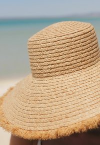Sombrero de paja de ala ancha en color natural, con textura tejida y borde con flecos, ideal para la protección solar.