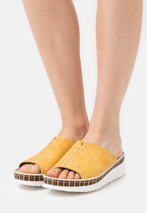 Yellow suede slide sandals with an open toe, featuring white stitching and a patterned wedge sole in brown and white.