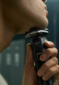 Rasoi elettrico Philips 5000 Series con manico ergonomico nero, testina argentata e pulsanti per l'operatività, posizionato su una superficie della pelle.