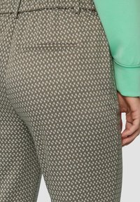 Brązowe spodnie w wzory z małym geometrycznym wzorem, z tylną kieszenią i gładką fakturą, zestawione z jasnooliwkową koszulą.