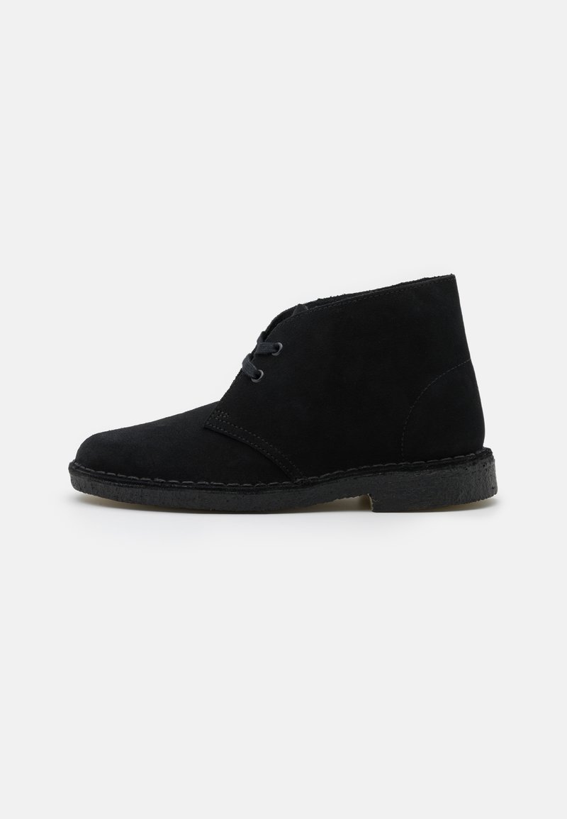 Schwarze Wildleder-Stiefelette mit runder Zehenpartie, zwei Schnürlöchern an der Seite und einer strukturierten Gummisohle. Minimale Nähte.