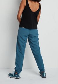 Top sin mangas negro, pantalones con cinturilla elástica azul y bolsillos laterales, y zapatillas deportivas turquesa con cordones; tejido texturizado y ajuste casual.