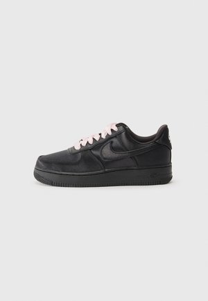 Baskets basses en cuir noir avec lacets rose clair, semelle noire et logo Nike swoosh sur un fond gris uni.