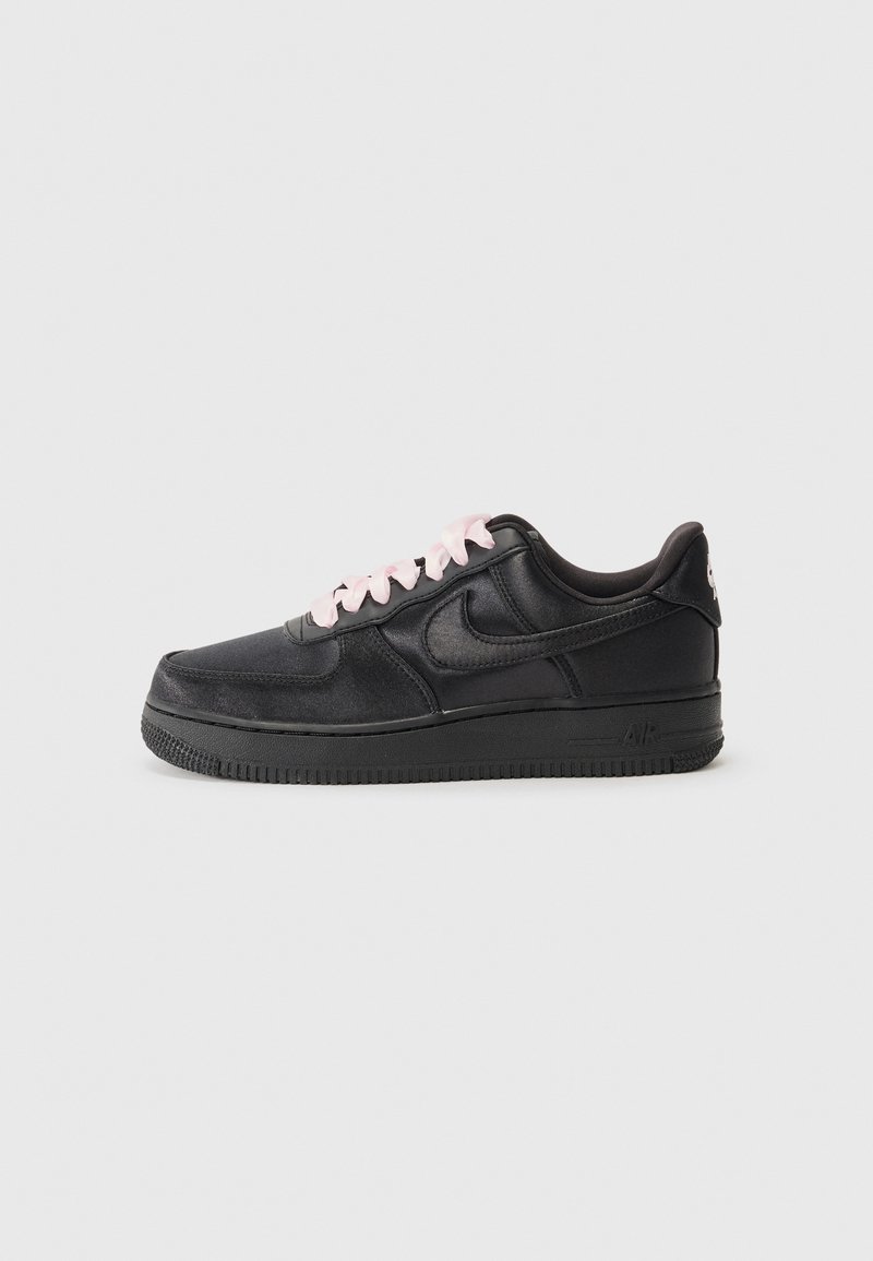 Baskets basses en cuir noir avec lacets rose clair, semelle noire et logo Nike swoosh sur un fond gris uni.