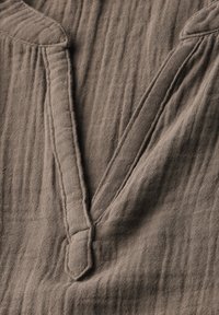 Brauner, strukturiert Stoff mit V-Ausschnitt-Design und dezenten Falten und Nähdetails, die ein weiches und geschichtetes Aussehen erzeugen.