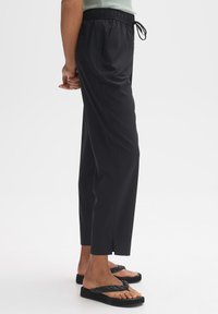 Schwarze, leichte Hose mit elastischem Bund und Kordelzug, seitlichen Taschen und einem geraden Schnitt, der sich an den Knöcheln leicht verjüngt.