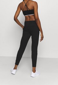 Svarta sportiga joggers i mjukt material, med smalnande ben-design, utrustade med elastisk midja, tillsammans med en svart kort topp och vita sneakers.