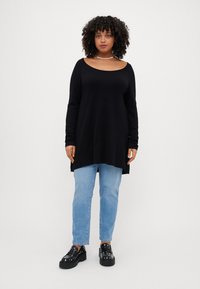 Black long-sleeve top with wide neckline, paired with light blue straight-leg jeans and black platform loafers with studded accents.