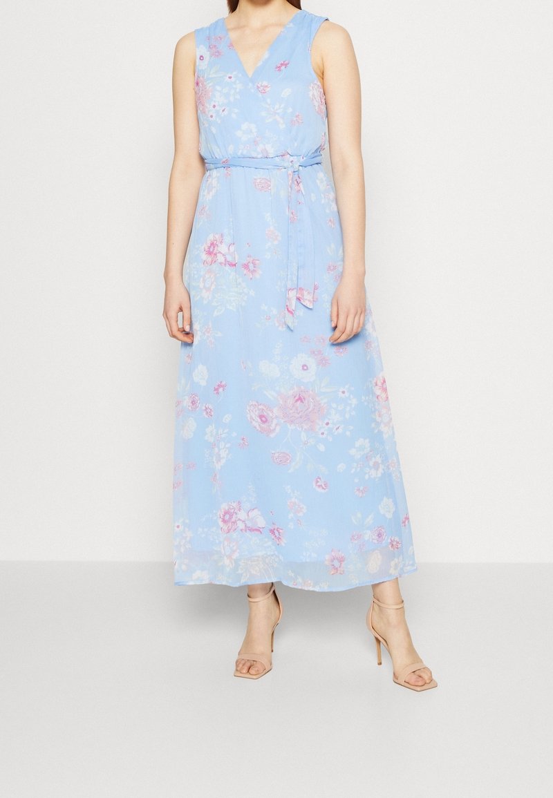 Ljusblå lång klänning med blommönster, v-ringning, ärmlös design och midjeband. Mjuk, flödande tyg framhäver formen.