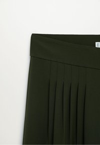 Tissu plissé vert foncé avec une large ceinture. Le matériau semble lisse avec une texture subtile, mettant en valeur des plis structurés et des lignes épurées.