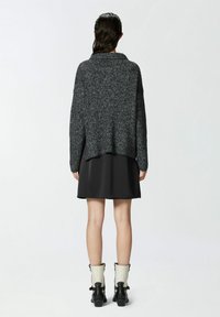 Abito nero all'altezza del ginocchio con un maglione grigio scuro dalla vestibilità ampia e texture, abbinato a stivaletti alla caviglia. Il maglione presenta un ampio colletto e spalle scese.