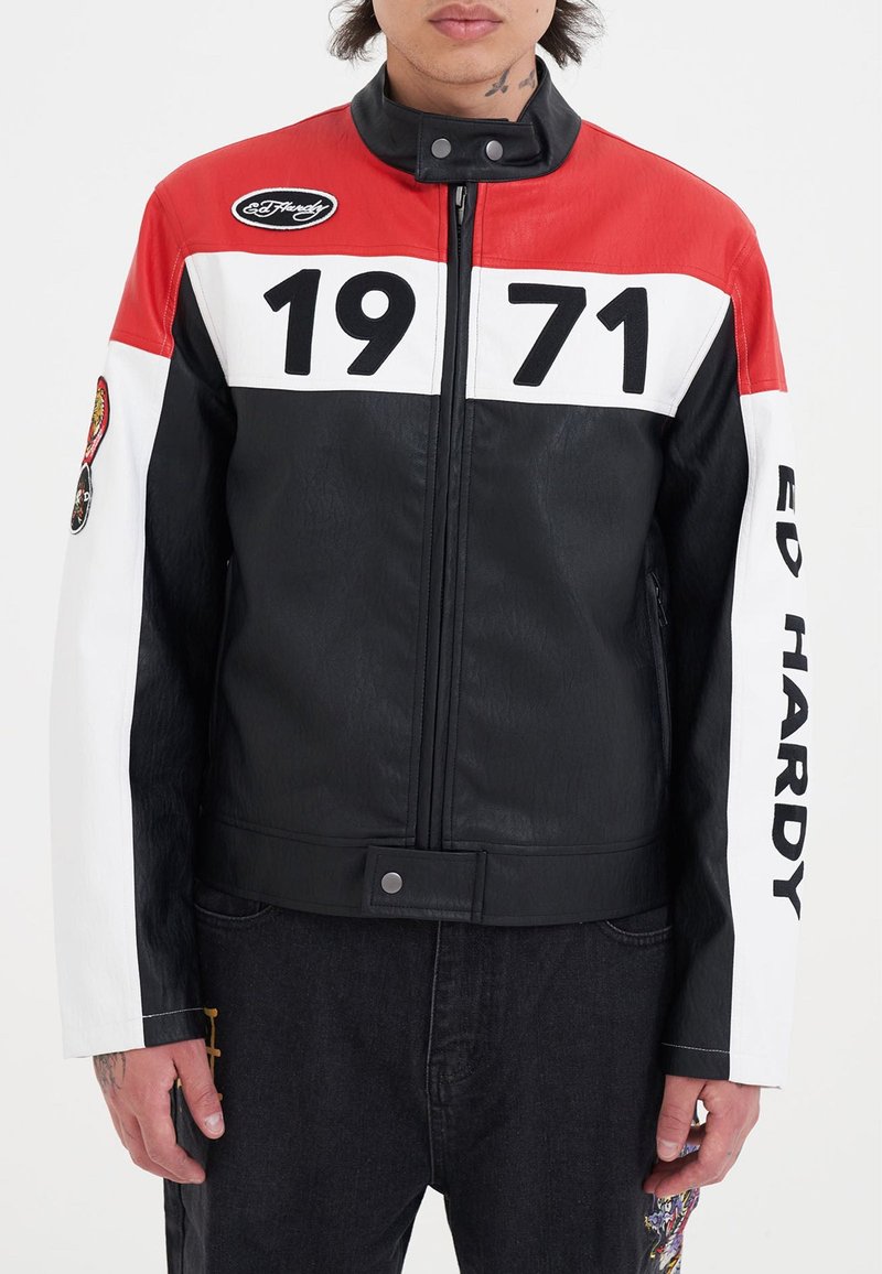 Svart läderjacka med röda, vita och svarta färgblock; har stor text "1971" och Ed Hardy-logotyp; inkluderar dekorativa lappar.
