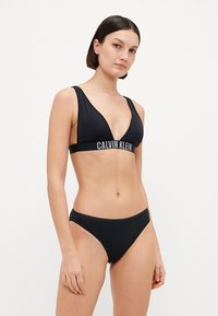 Fekete bikini szett, háromszög alakú bralette-tel, Calvin Klein márkajelzéssel és passzoló, alacsony derekú alsó résszel, sima anyagból.