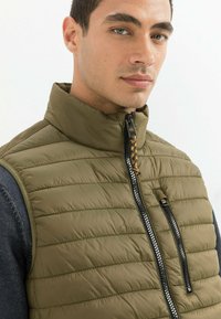 Olivgrüne Daunenweste mit hohem Kragen, im horizontalen Steppdesign, schwarzem Reißverschluss und seitlichen Taschen mit strukturierten Akzenten.