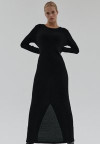Czarna prążkowana sukienka dzianinowa z długimi rękawami, prostą sylwetką i trójkątnym wycięciem u dołu. Miękka faktura z gładkim wykończeniem.