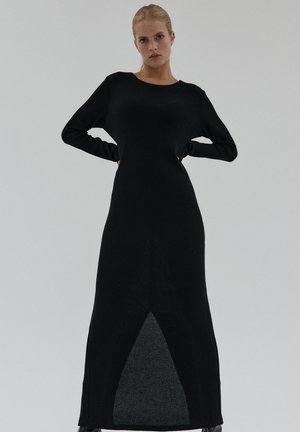 Czarna prążkowana sukienka dzianinowa z długimi rękawami, prostą sylwetką i trójkątnym wycięciem u dołu. Miękka faktura z gładkim wykończeniem.
