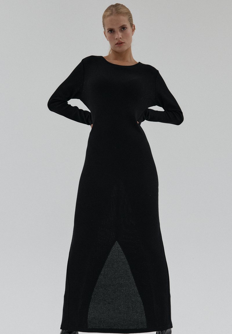 Czarna prążkowana sukienka dzianinowa z długimi rękawami, prostą sylwetką i trójkątnym wycięciem u dołu. Miękka faktura z gładkim wykończeniem.