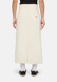 Beige knälång kjol i bomullstyg, med en centrerad bakre slitsömm, två sidofickor i cargo-stil och en logotyp-patch på baksidan.