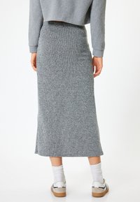 Gonna grigia a costine con vita aderente e spacco laterale, abbinata a calzini bianchi e scarpe casual, che mette in mostra un tessuto testurizzato.