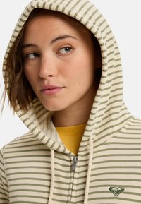 Sudadera con cremallera a rayas en color beige claro y verde, con capucha ajustable y un pequeño logo bordado en el pecho. Material de mezcla de algodón.