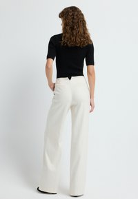 Czarna, prążkowana bluzka z krótkim rękawem i rozcięciem z tyłu, w połączeniu z lekkimi, w kolorze śmietankowym, spodniami o wysokim stanie i szerokich nogawkach, ozdobionymi delikatnymi paskami.