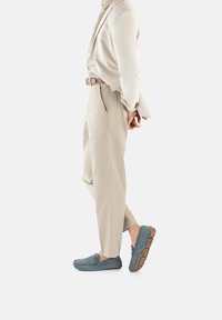 Jasnoniebieskie zamszowe loafersy z gumową podeszwą i dekoracyjnym przeszyciem, zestawione z jasnobeżowymi, dopasowanymi spodniami i odpowiadającą marynarką.