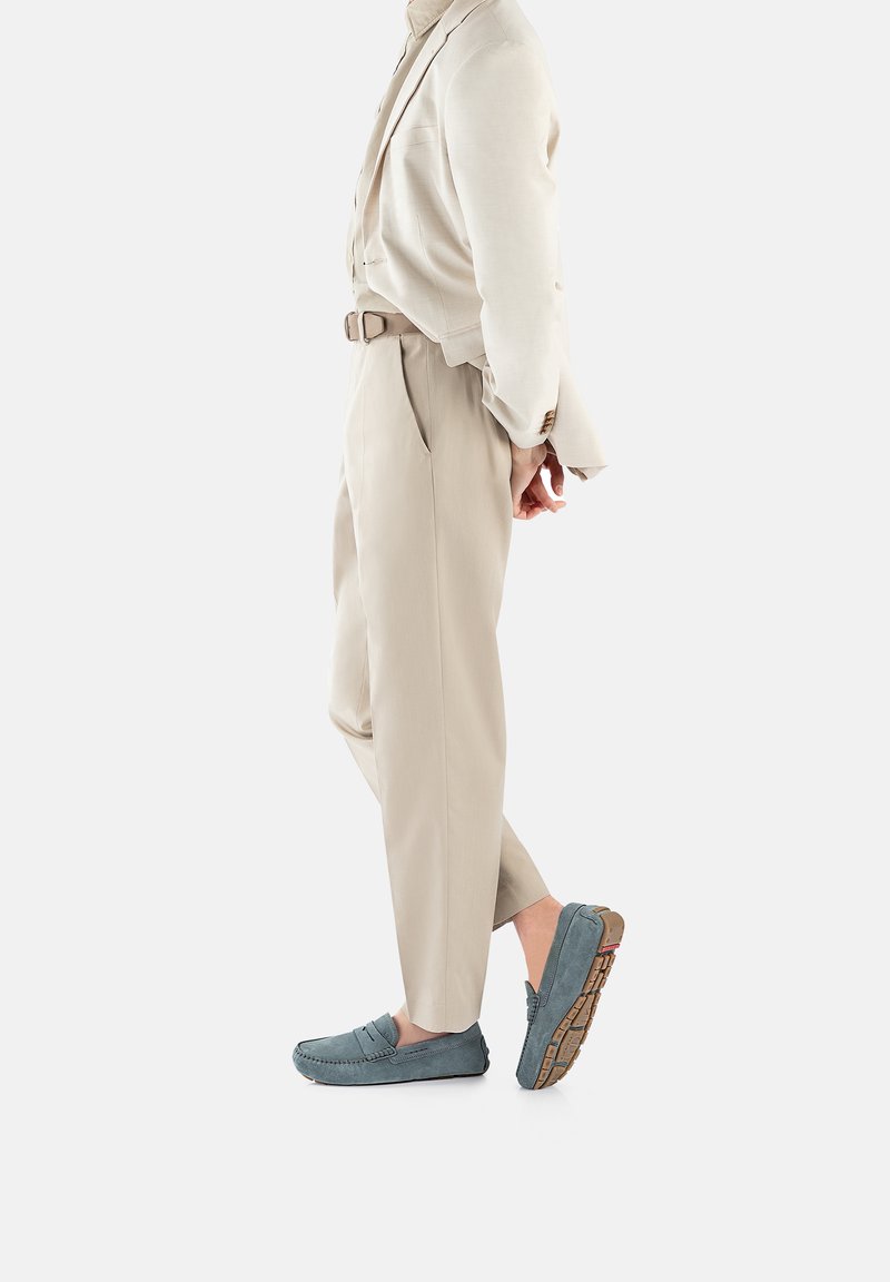 Jasnoniebieskie zamszowe loafersy z gumową podeszwą i dekoracyjnym przeszyciem, zestawione z jasnobeżowymi, dopasowanymi spodniami i odpowiadającą marynarką.