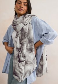 Gray and white patterned scarf with a textured, ribbed design, draped stylishly around the neck of a person wearing a blue striped shirt.