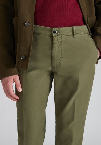 Oliwkowe spodnie o dopasowanym kroju, wykonane z bawełnianego twillu. Posiadają zapięcie na guzik z przodu oraz kieszenie boczne. Uzupełnione brązową kurtką.