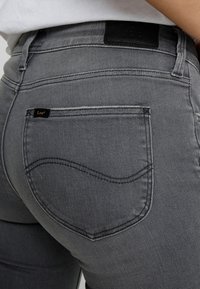 Jeans de mezclilla gris con una cintura alta, que cuentan con un bolsillo trasero con una costura curva y una etiqueta de cuero negro en la cintura.
