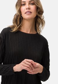 Fekete, hosszúujjú felső, textúrált függőleges redőkkel. Kerek nyakkivágás, puha anyag és testhezálló dizájn, redős ujjakkal.