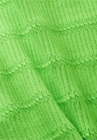 Jasnozielona dzianina o żebrowej teksturze i ściegach w zygzak, tworząca subtelne przekątne fale na materiale.